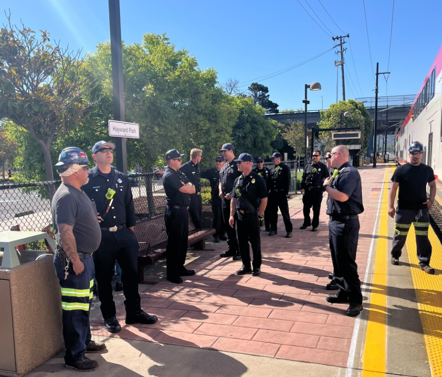 A dozen firefighters stand on the platform of the Hayward Park station outside the new upcoming electric train, ready to learn new safety information.