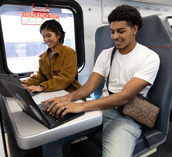 Two young people using their laptops on the train