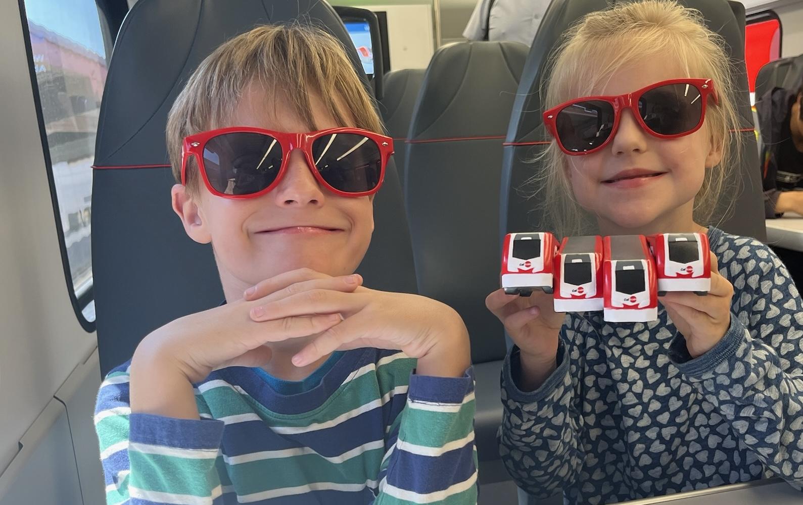 Two adorable kids show off Caltrain swag while sitting on an electric train